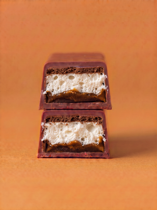 Two stacked chocolate-covered bars with a white airy cream filling and caramel brown base, set against a solid warm orange background.